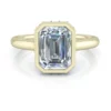 Yellow Gold Emerald Cut Bezel Ring Setting with Under Halo - Style GTJ3908-emerald-y-8x6mm-1 A bezel set emerald cut diamond in yellow gold. Accented by a hidden halo and laying on flat white reflective surface.