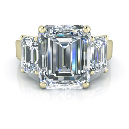 Three stone emerald cut engagement ring in yellow gold laying on flat surface.